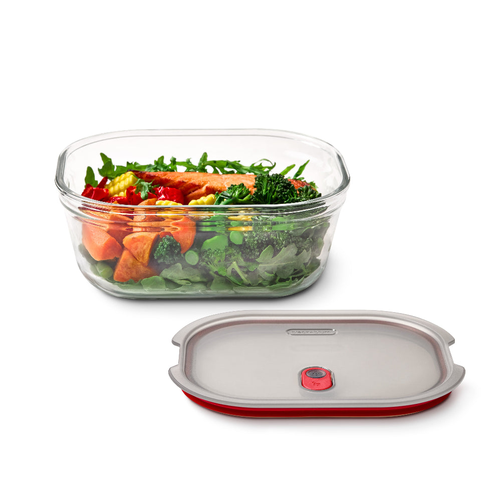A clear glass rectangular storage container filled with mixed vegetables, shown with its detached lid below on a white background. The lid has a gray top surface, a red edge, and a small red circular seal.